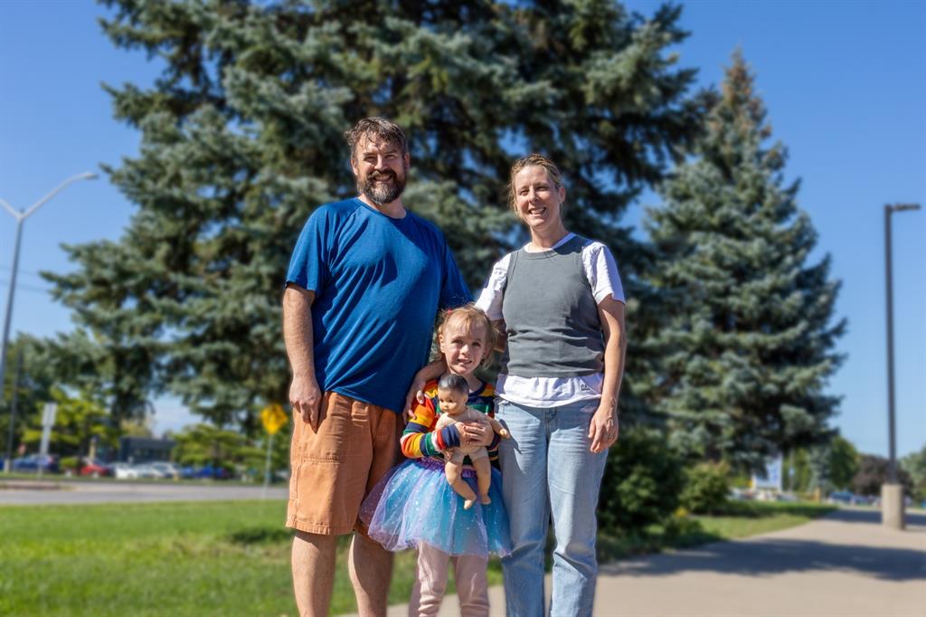 Man, women and young girl stand in front of evergreen tree